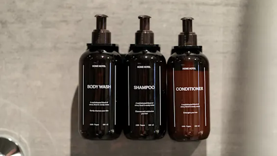 Tre flaskor märkta BODY WASH, SHAMPOO och CONDITIONER är monterade på en vägg, redo att användas.