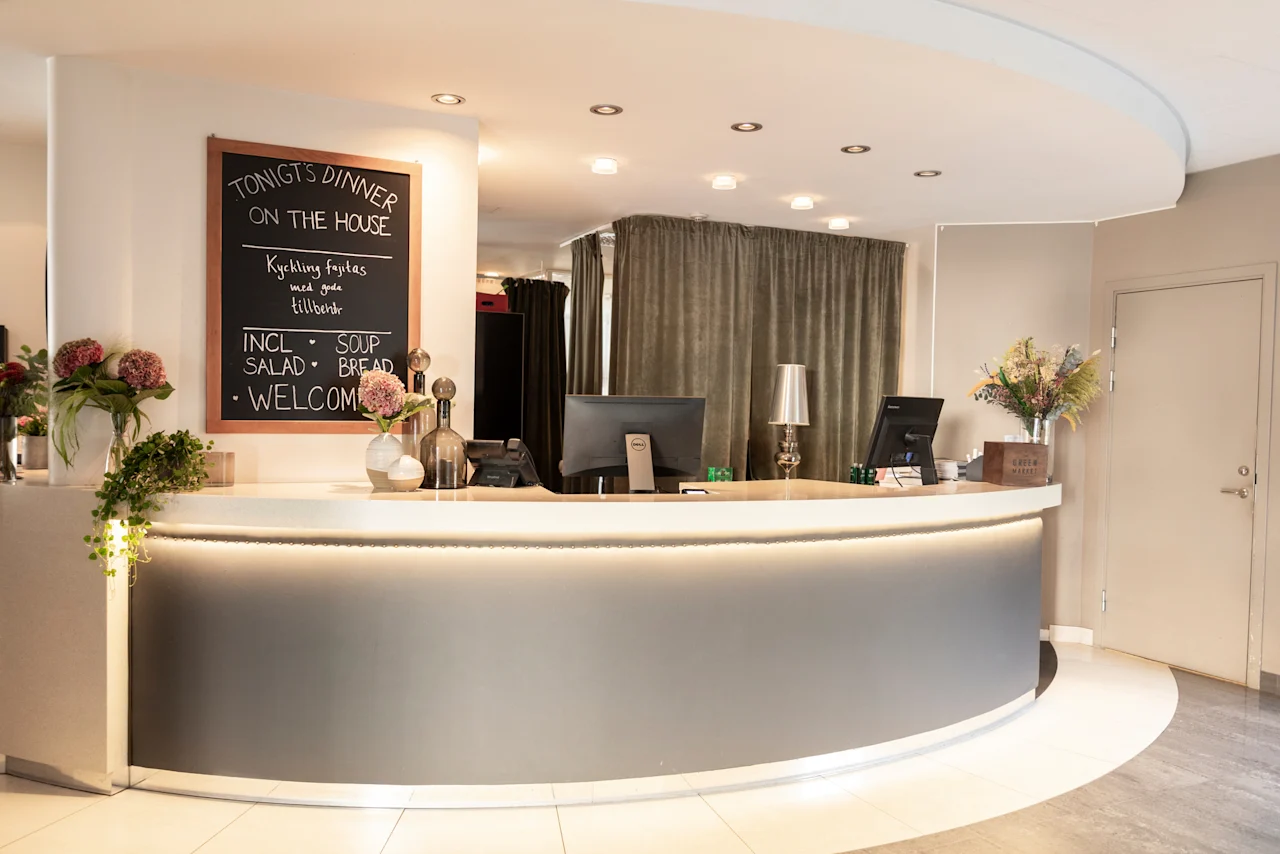 En hotellreception med en svart tavla som annonserar TONIGTS DINNER ON THE HOUSE och en meny.