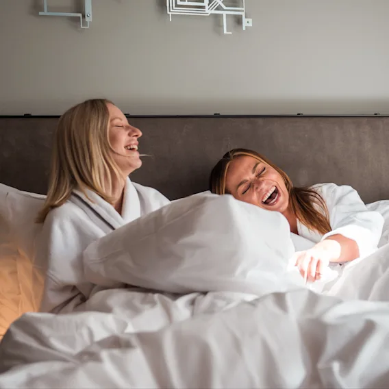 Two people in bathrobes laughing joyfully in bed.