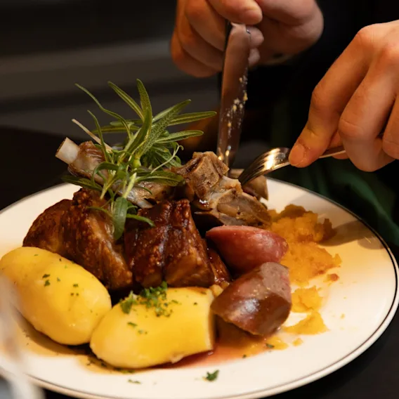 Hender som skjærer i en tallerken med tradisjonell norsk julemat bestående av ribbe, pølse og poteter.