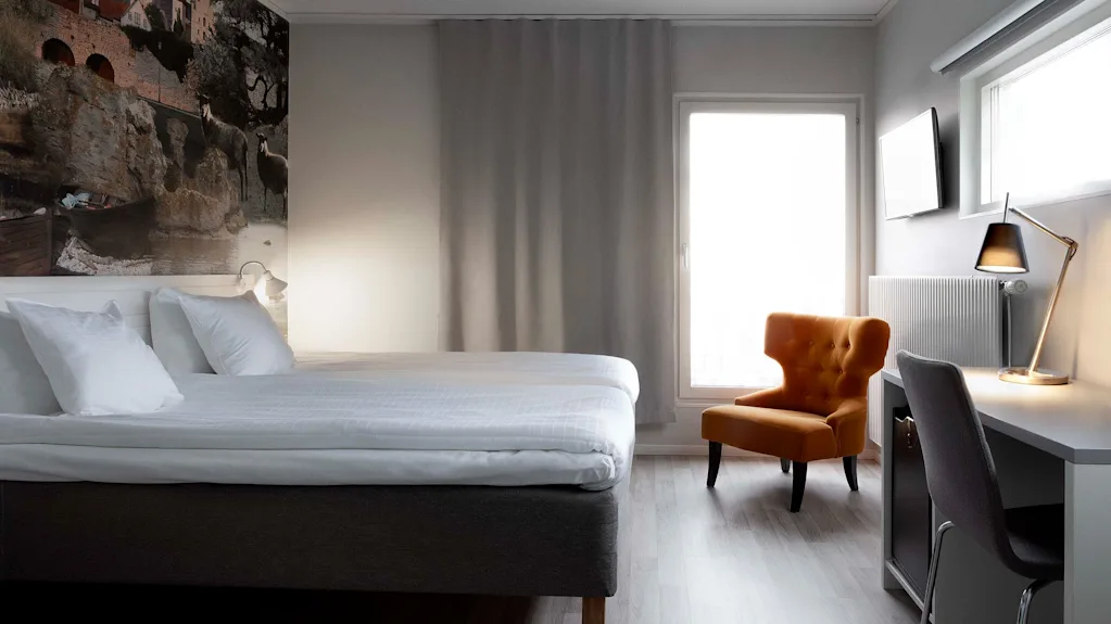 Ett ljust och inbjudande hotellrum med en bekväm säng, en mysig fåtölj och en funktionell skrivbordsplats.