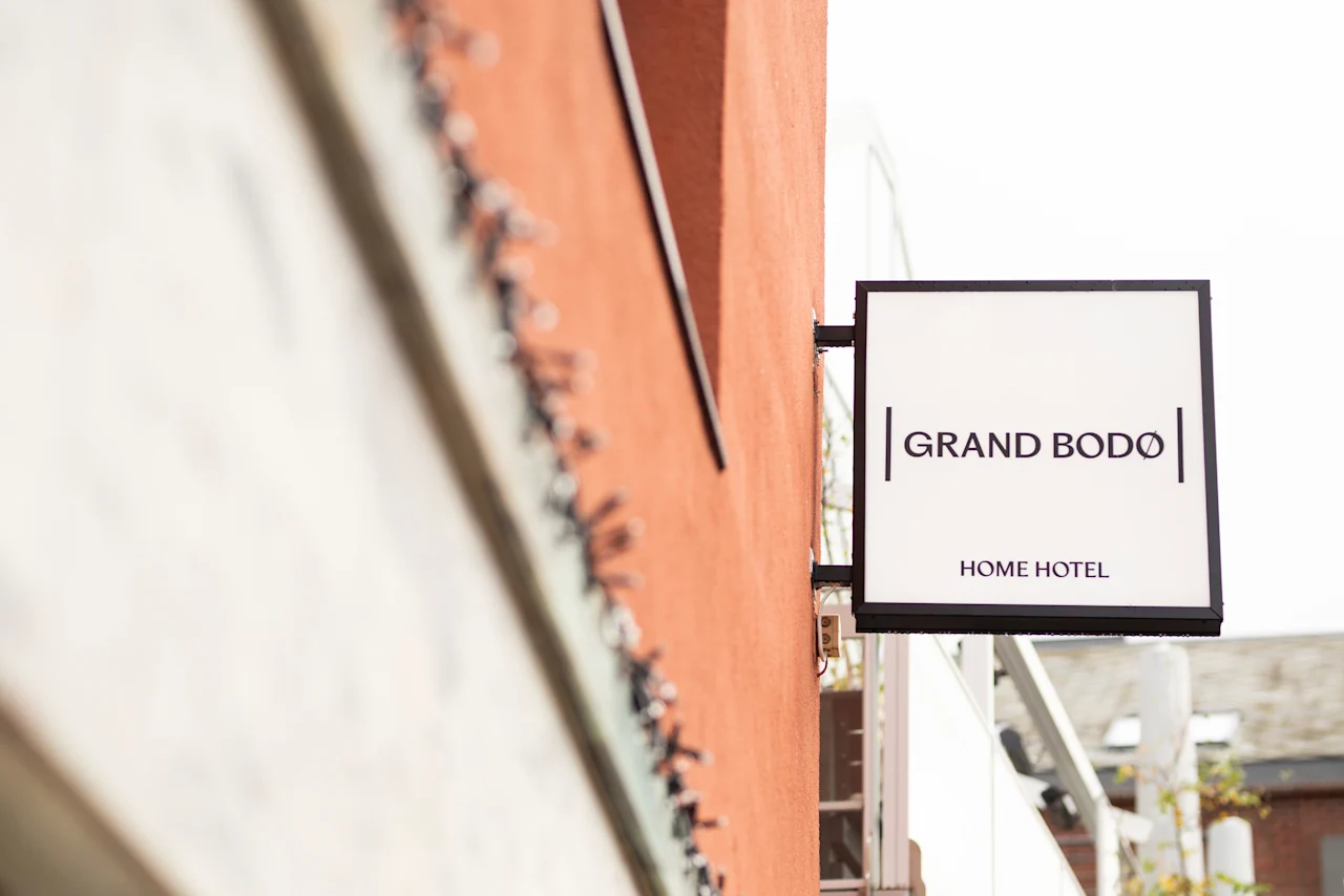 A white sign for Home Hotel Grand Bodø hangs on an orange building.