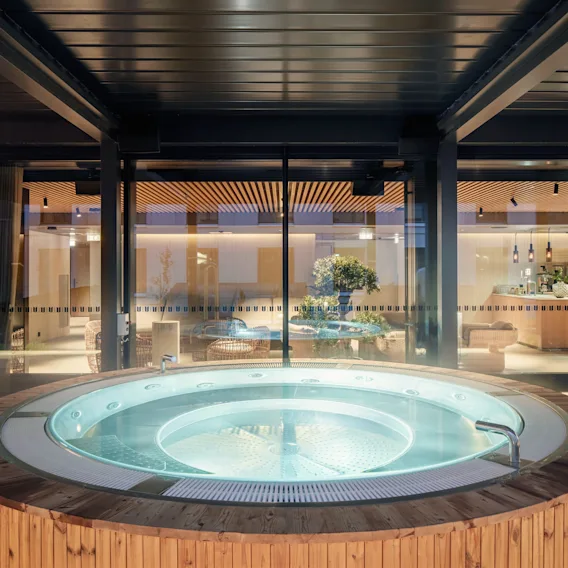 Spa Clarion Hotel Helsinki Airportissa. Pyöreä poreallas kirkkaalla vedellä puukannella, josta on näkymä moderniin sisäoleskelutilaan.