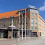 Et fleretagers hotel med rødt tegltag står på en solrig gade, med skilte der viser "QUALITY HOTEL THE REEF" på facaden. Flere flag er placeret foran.