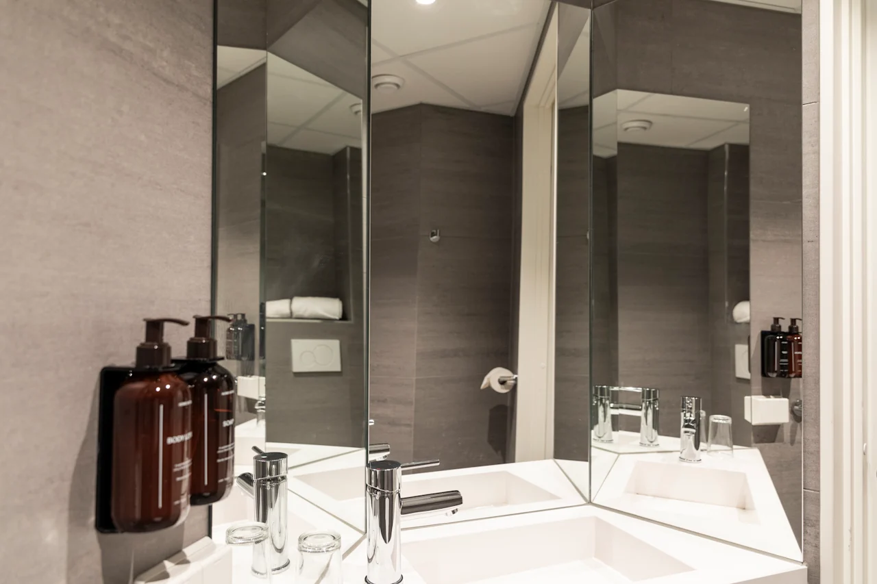 A modern and clean bathroom featuring a double sink, sleek faucets, and multiple mirrors, with toiletries neatly arranged.