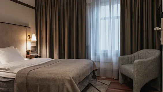 Et hyggeligt hotelværelse med en komfortabel seng, en varm lampe og et vindue med lette og mørklægningsgardiner.