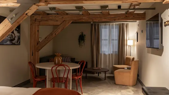 Et koselig oppholdsrom med synlige trebjelker, et spisebord og en komfortabel sittegruppe.