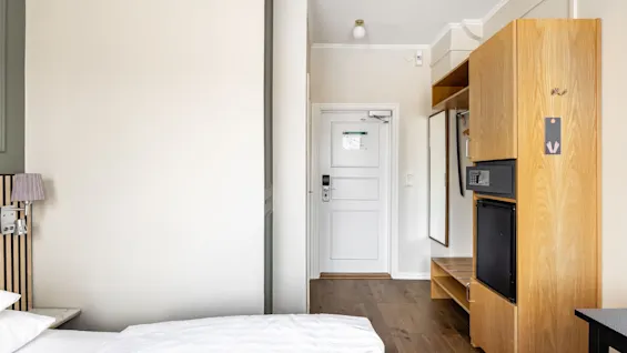 Viihtyisä hotellihuone Comfort Hotel Linköping Cityssä sängyllä, vaatekaapilla, tallelokerolla ja minibaarilla, valmiina mukavaan oleskeluun.