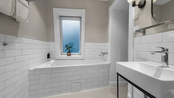 A bright and clean bathroom featuring a bathtub under a window and a modern sink, designed for a refreshing experience.