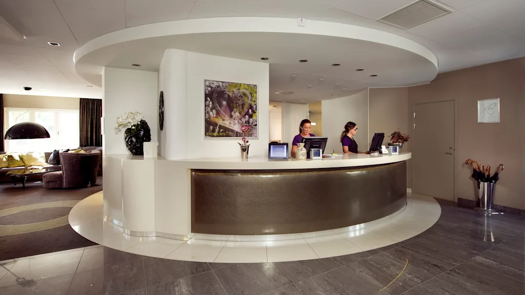 Two staff members work at a curved reception desk in a modern hotel lobby.