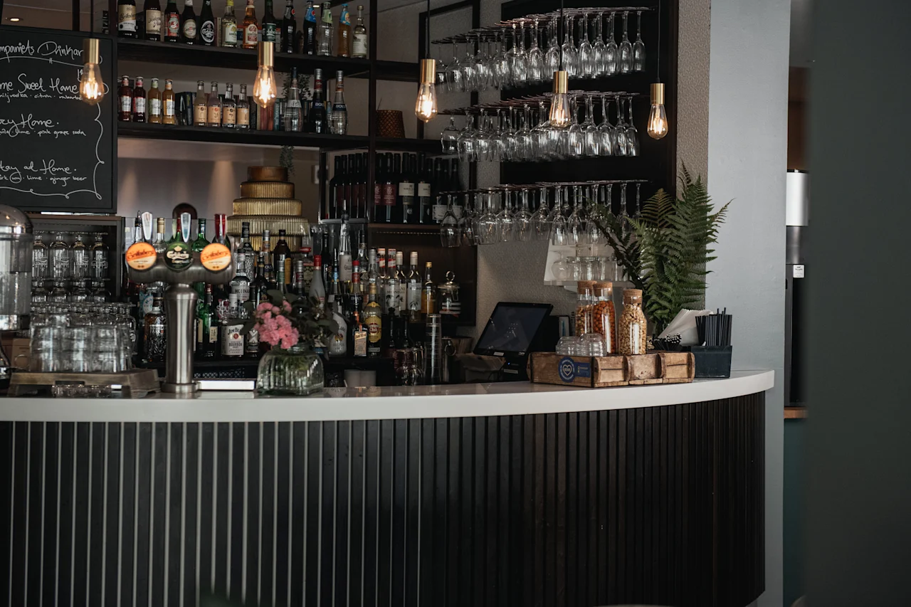 En stilren bar med flaskor, hängande glas, ölkranar och en griffeltavla som säger Home Sweet Home, Stay Home, Stay at Home.