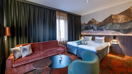 A stylish hotel room with a mountain mural, elegant furniture, and coordinated colors.