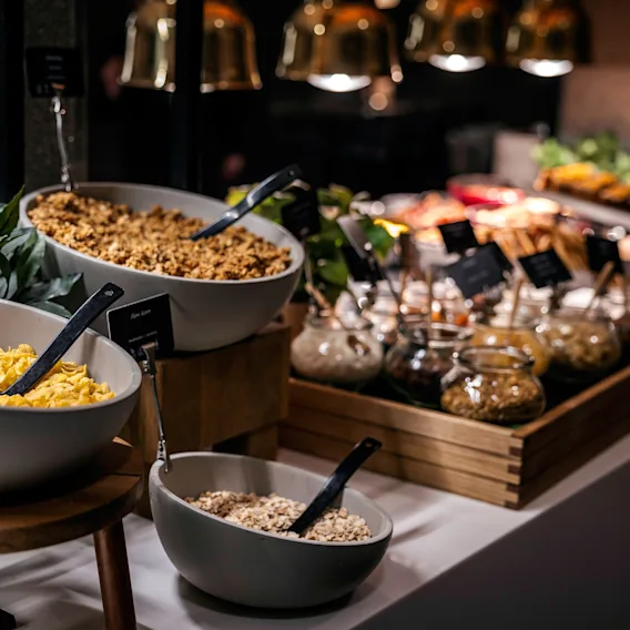 En frokostbuffé med skåler med frokostblandinger og havre, sammen med diverse tilbehør i små glasskrukker, klart for gjester.