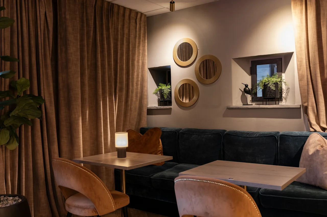 Cozy seating area with dark blue sofa, wooden tables, and warm lighting at Home Hotel Grand Bodø.
