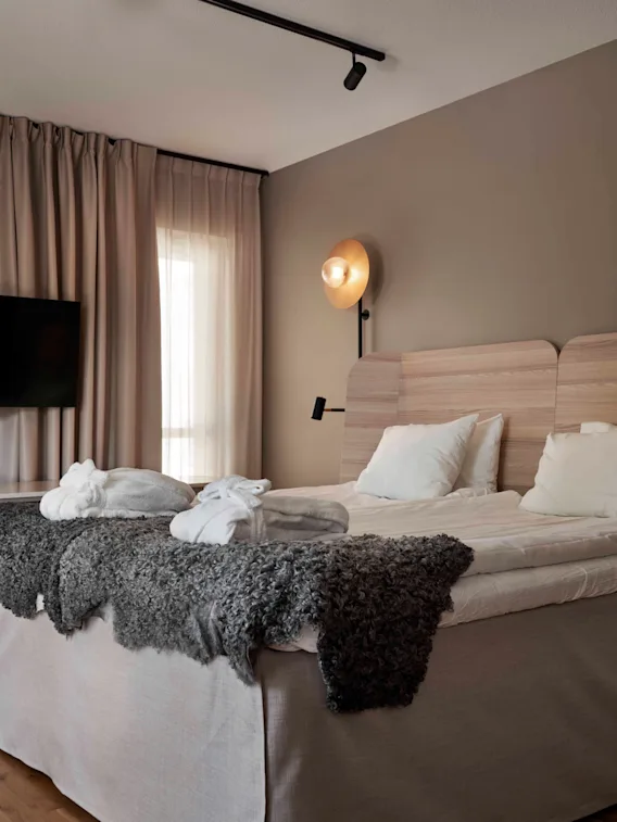A modern and inviting hotel room featuring a large bed with bathrobes, a wall-mounted TV, and warm lighting.