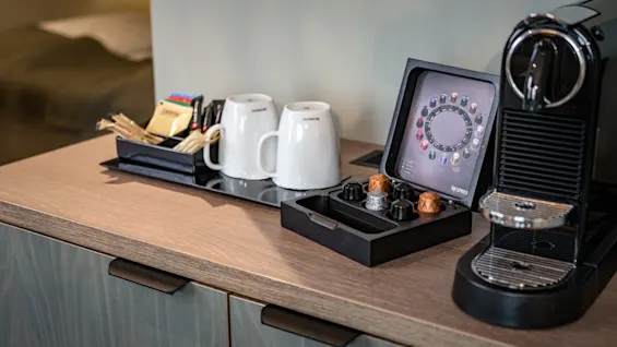 En kaffestasjon med en maskin, krus og forskjellige kaffekapsler, klar for en varm drikke.