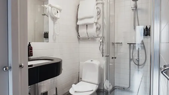 Et rent og funktionelt hotelbadeværelse på Home Hotel Wellington, med håndvask, toilet og en glasindkapslet bruser.