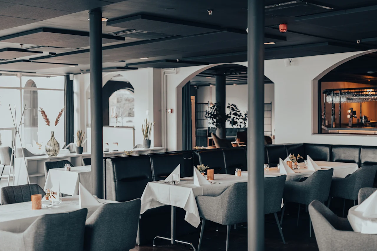 En modern restaurangmiljö med dukade bord, vita dukar och eleganta mörka stolar.