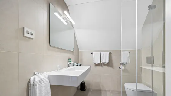 A modern bathroom with a sink, mirror, towel, and glass shower stall.