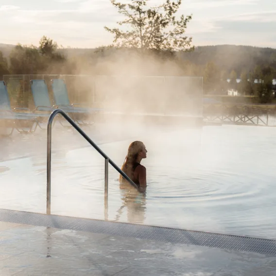 En person kopplar av i en ångande utomhuspool på ett spa med vacker utsikt.