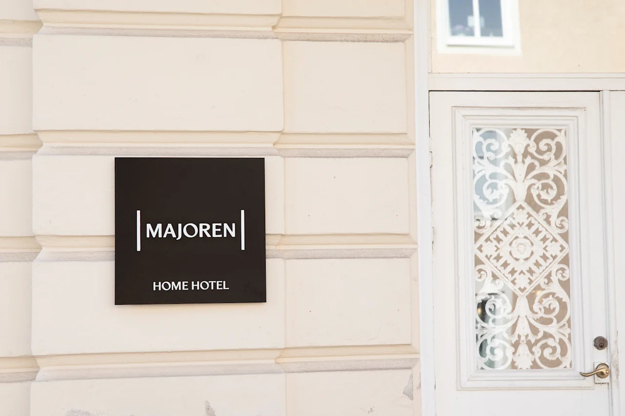 Rakennuksen ulkokuva, jossa kyltti MAJOREN HOME HOTEL koristeellisen valkoisen sisäänkäyntioven vieressä.