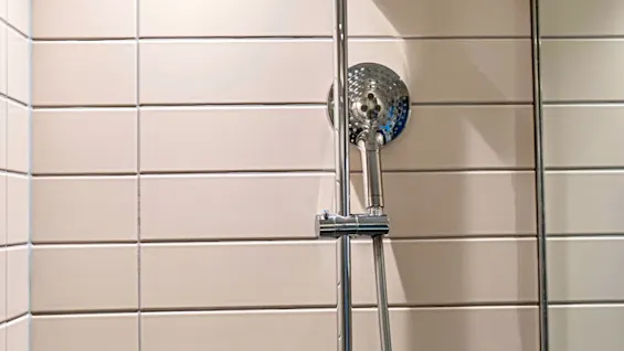 En modern dusch med takdusch, handdusch och en väggmonterad dispenser märkt HAIR & BODY.