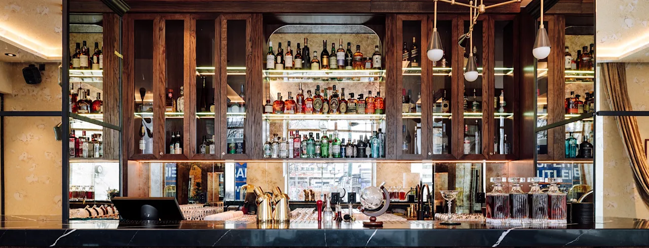 En velfylt bar med mange spritflasker på hyller, en marmordisk og barverktøy, som skaper en innbydende atmosfære.