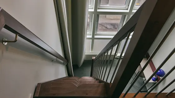 A downward view of a wooden staircase with a handrail and banister, illuminated by a large skylight above.