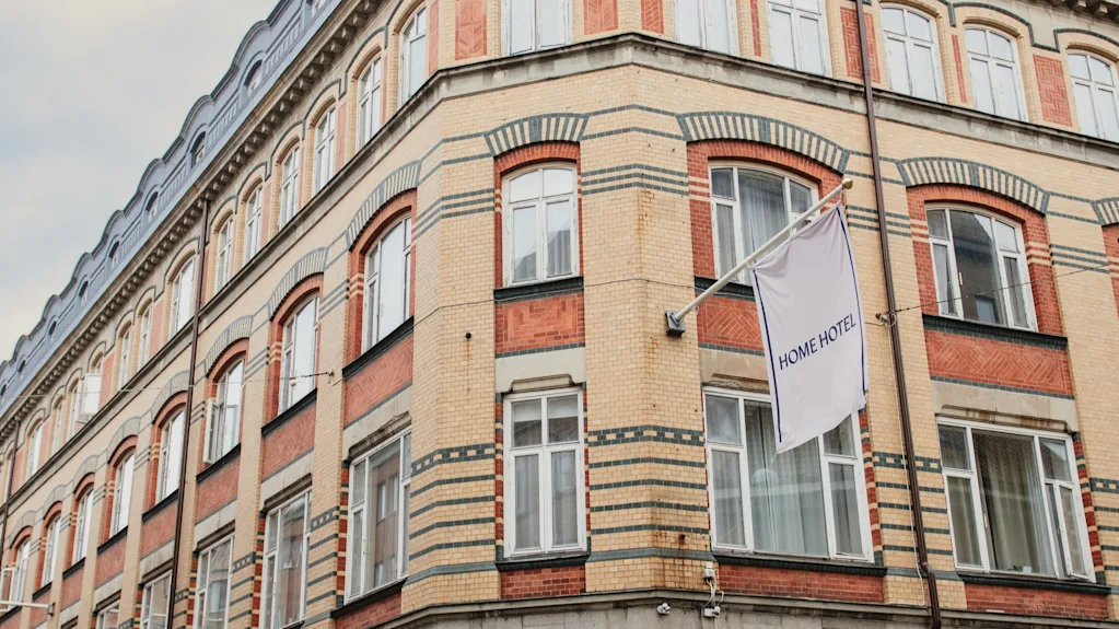 En fleretagers bygning med buet tag og murstensfacade. Et flag viser HOME HOTEL, og et vinduesskilt lyder TEMPERANCE HOME HOTEL.