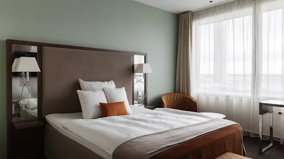 Et indbydende hotelværelse med en komfortabel seng, elegante møbler og et stort vindue, der giver rigeligt lys.