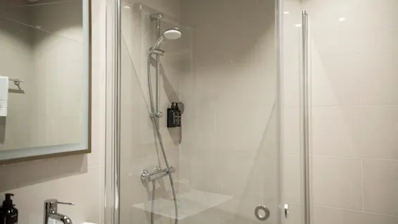 Et rent og moderne badeværelse med en brusekabine med glasdøre, en vask og et spejl.