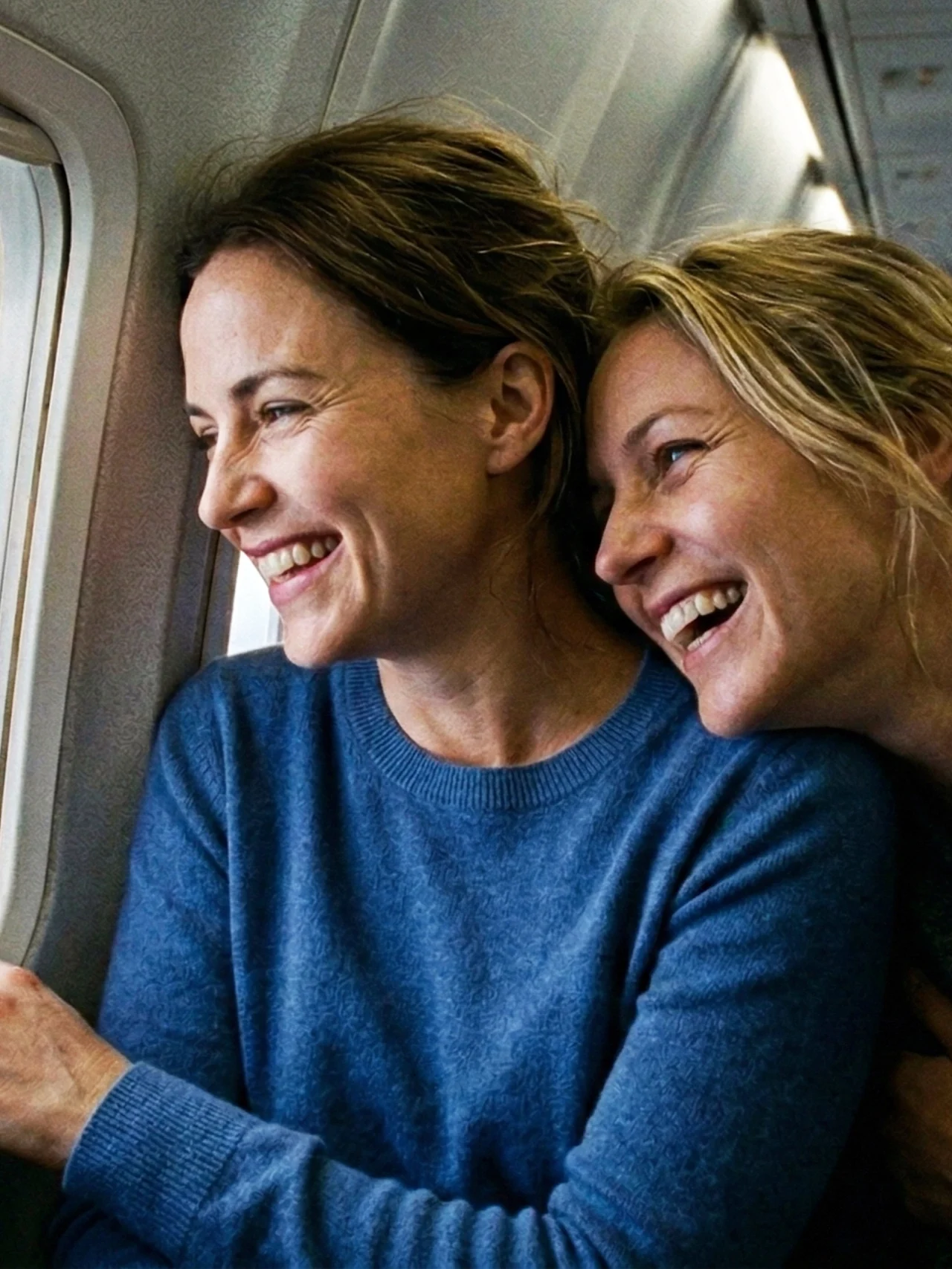 Två glada personer tittar ut genom ett flygplansfönster och njuter av utsikten och varandras sällskap.