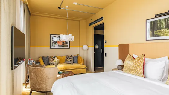 Et levende hotelværelse på Hernö Gin Hotel med en hyggelig seng, en komfortabel gul sofa og moderne indretning.