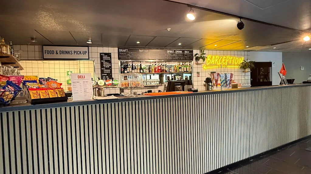 En modern bar- och receptionsdisk med snacks, drycker och skyltar för mat- och dryckesupphämtning samt delitjänster.