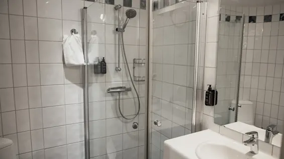 Et rent og moderne badeværelse med et flisebelagt bruseområde og en håndvask. Vigtige toiletartikler er tilgængelige for en forfriskende oplevelse.