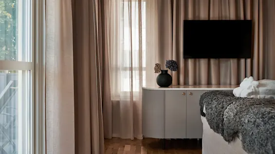 Ett inbjudande hotellrum med varmtonade gardiner, en bekväm säng, en TV och ett stilrent skåp.