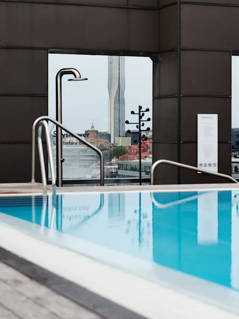 A rooftop swimming pool with a shower and city skyline in the background. Text reads: Syshower before b.