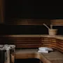 A cozy wooden sauna interior with benches, a bucket and ladle, a heater, and fresh white towels, ready for relaxation.