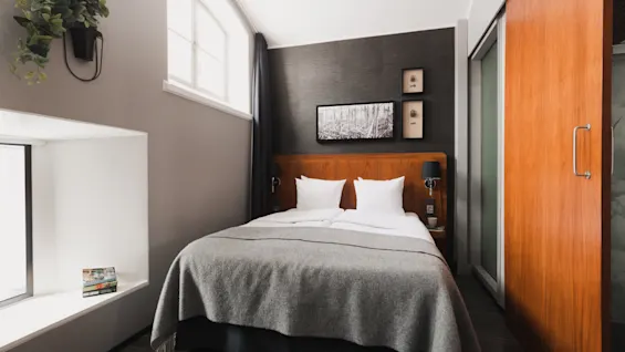 Et komfortabelt hotelværelse med en stor seng, en plante og kunstværker, med et unikt buet vindue og en skydedør i træ.