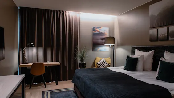 Et koselig hotellrom med en komfortabel seng, et funksjonelt skrivebordsområde og varm belysning, som skaper en avslappende atmosfære.