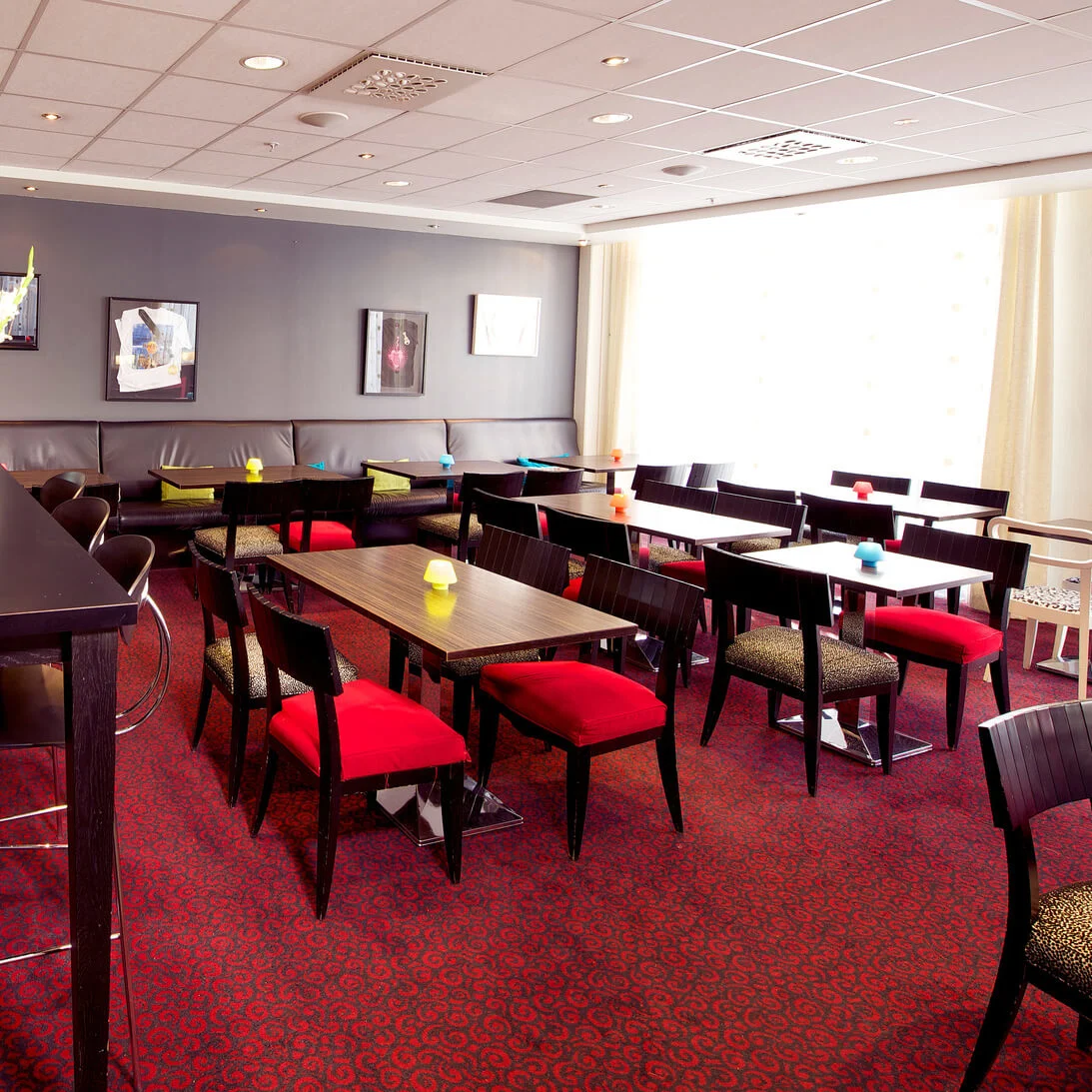 An interior of a modern cafeteria with black tables and chairs, with red accents, under white ceiling lights.