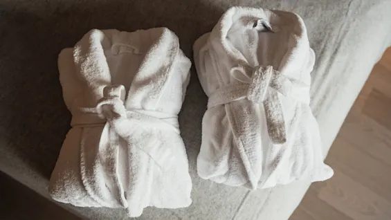 Two fluffy white bathrobes neatly folded on a bed, ready for use, suggesting comfort and relaxation.