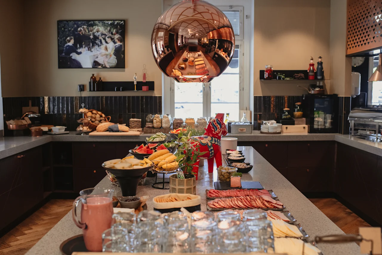 En livlig buffé med fersk frukt, pålegg og bakverk, servert i et lyst spiseområde med en stor sfærisk lysarmatur.