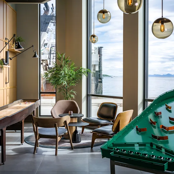 Et livlig loungeområde på Quality Hotel Harstad med shuffleboard, flipperspill og sitteplasser, med fantastisk sjøutsikt.