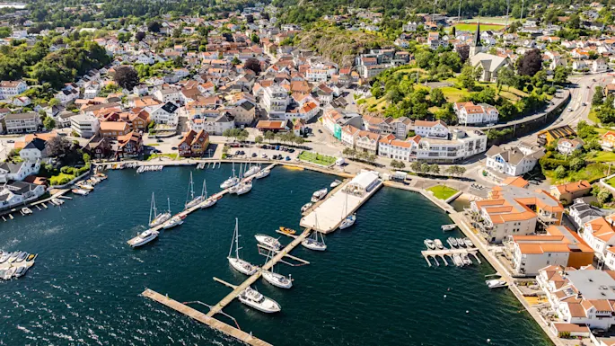 Aerial view of a coastal town with boats docked at piers, surrounded by dense buildings and green hills.