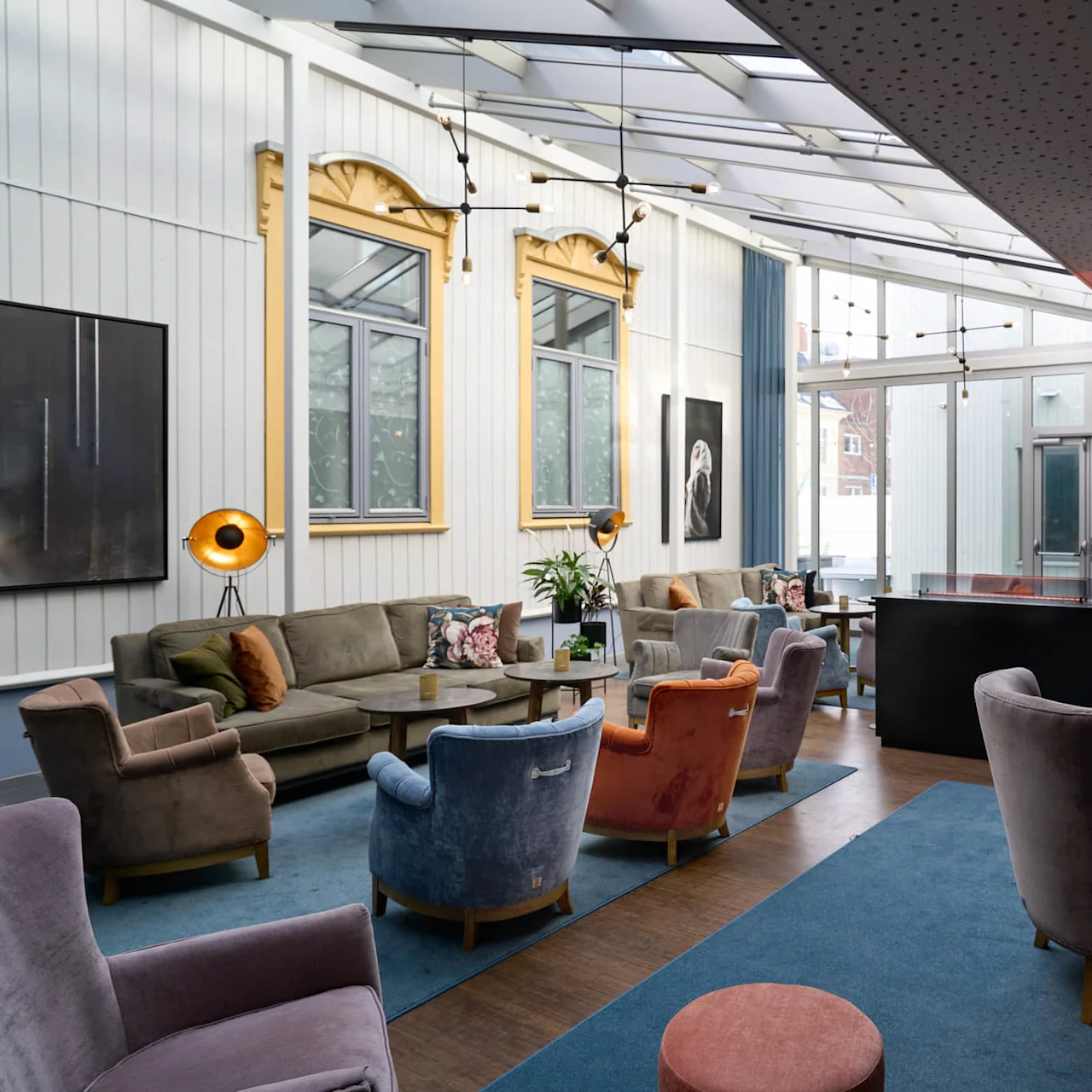 En elegant lounge med bløde siddepladser og dekorativ belysning, prydet med kunstværker og store vinduer, udstråler en hyggelig, luksuriøs atmosfære.