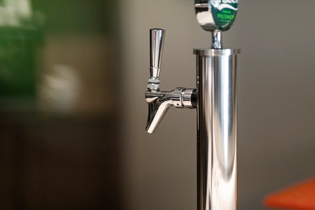 Close-up of a polished metal drink dispenser with a handle, featuring a label that says Pilsner.