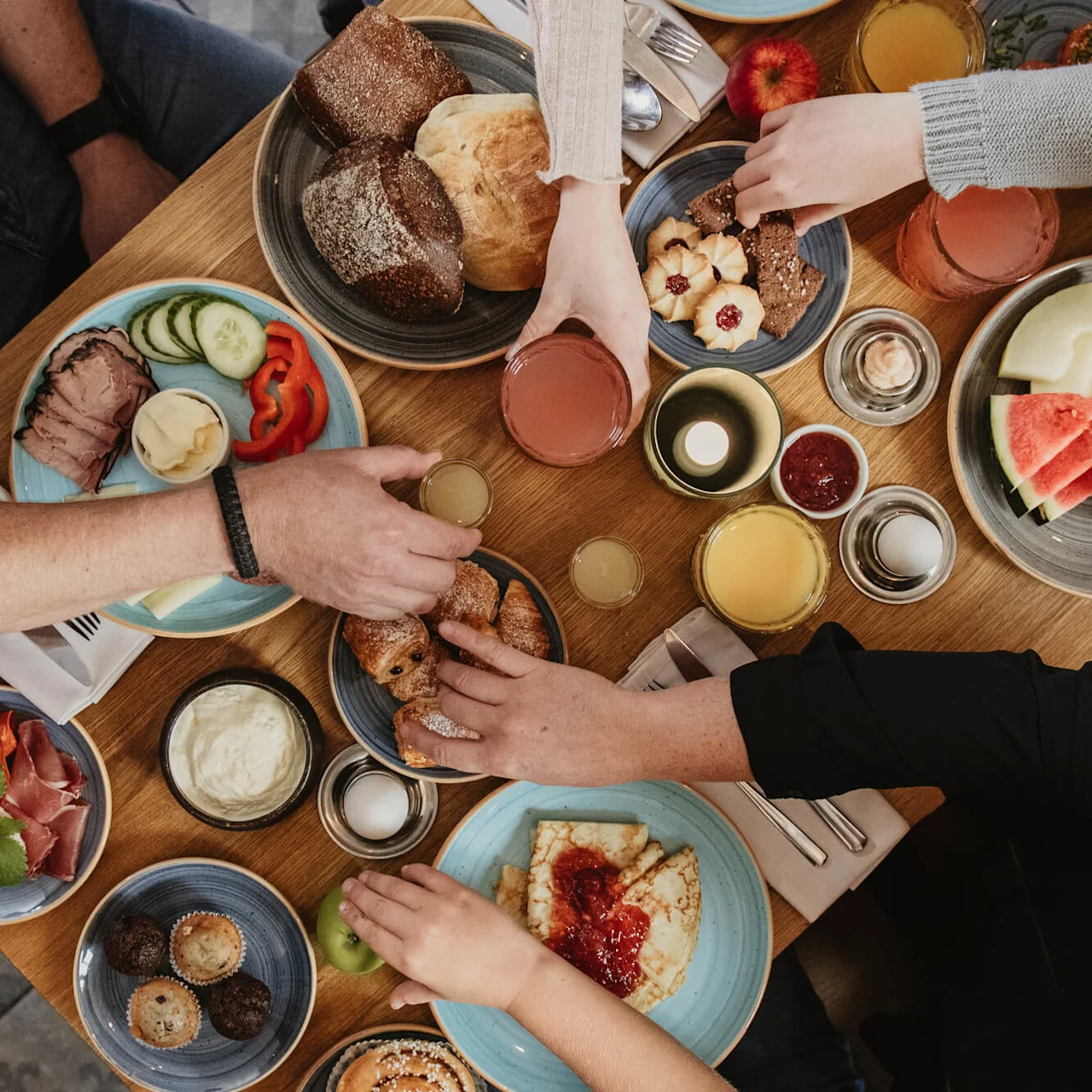 Personer spiser frokost sammen, deler ulike retter, oversiktsbilde over et trebord.