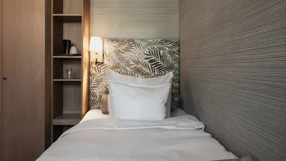 En hyggelig enkeltseng med en bladmønstret sengegavl og en træhylde i et værelse på Home Hotel Wellington.