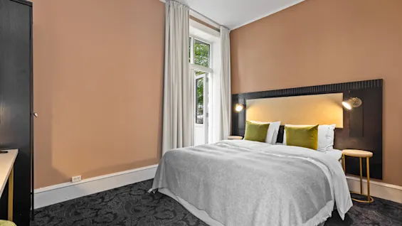 Et koselig hotellrom på Home Hotel Gabelshus med en komfortabel seng, varm belysning og utsikt over grøntområder fra vinduet.